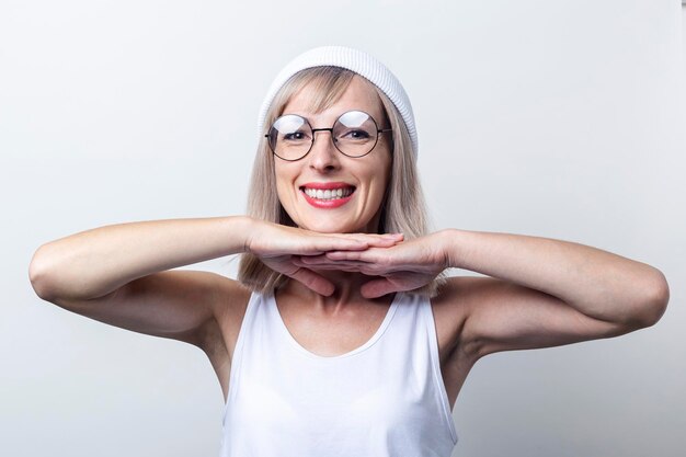 Cheerful young woman holds her palms under the chin on a light background