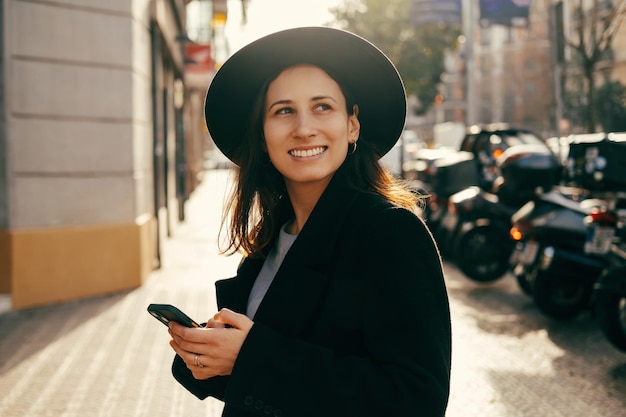 Cheerful young woman holds her phone while walking down the European streets