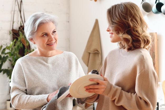 Cheerful young woman hugging aged mother sitting on sofa while resting together in living room at home