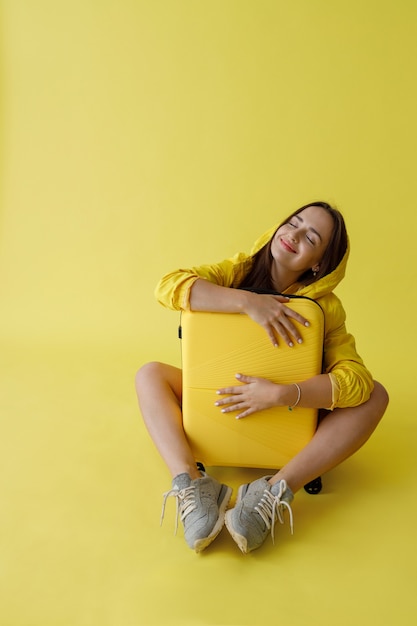 Cheerful young woman hugging travel bag in studio