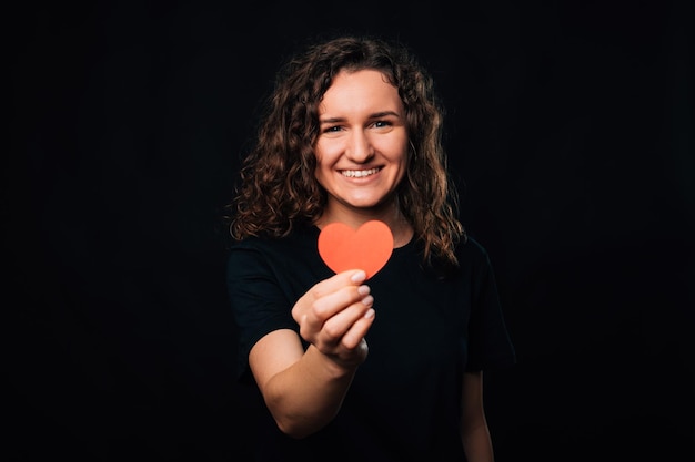 Cheerful young woman is holding a red paper heart for love and goodness