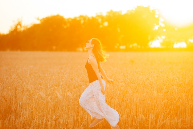 Cheerful young woman is running on a crops field on a sunny day.