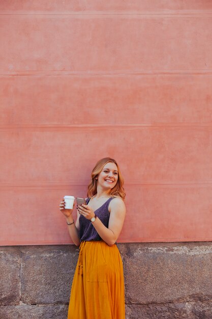 Cheerful young woman isolated on a wall using her phone