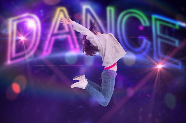 Photo cheerful young woman jumping against digitally generated colourful dance text