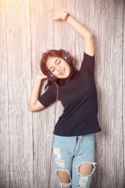 Cheerful young woman listening music wearing headphones with wall background.