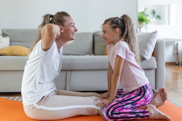 Cheerful young woman and little girl in sportswear exercising together in modern light room mother and daughter practicing yoga
