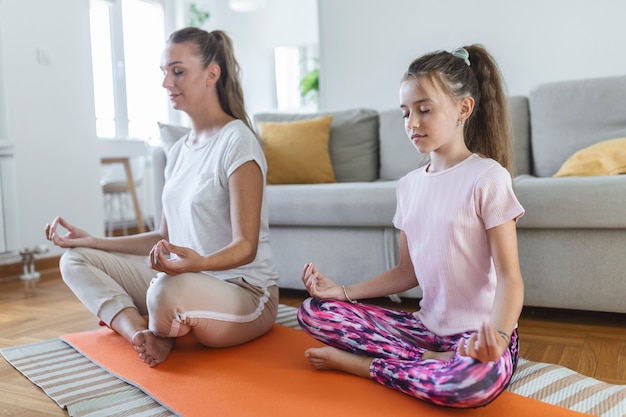 cheerful young woman and little girl in sportswear exercising together in modern light room. mother and daughter practicing yoga