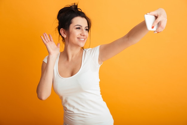 Cheerful young woman make selfie by mobile phone waving.