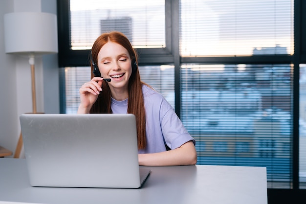 Cheerful young woman operator using headset and laptop computer\
during customer support at home office.