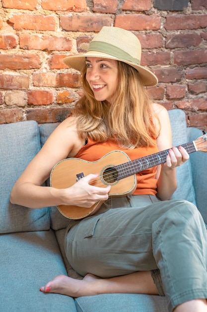 Фото Веселая молодая женщина играет на укулеле на диване в уютном доме в стиле бохо