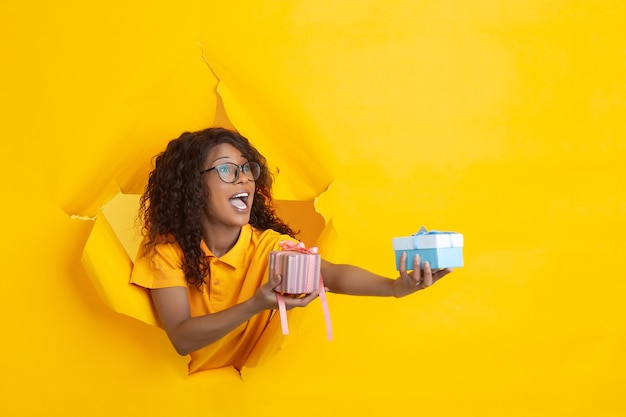 Cheerful young woman poses in torn yellow paper hole background emotional and expressive