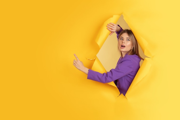 Una giovane donna allegra posa in un buco di carta gialla strappata, emotiva ed espressiva