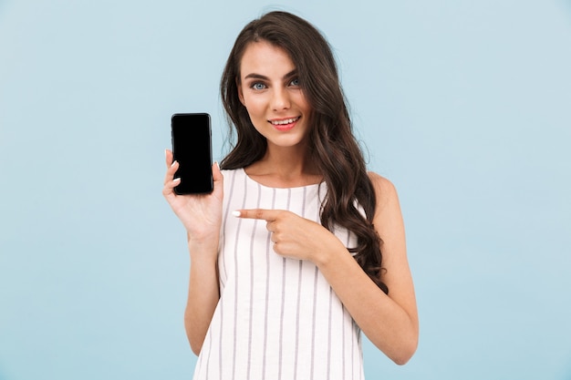 Cheerful young woman posing isolated wall showing display of mobile phone pointing.