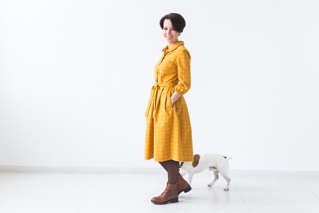 Cheerful young woman posing in a yellow dress with her beloved dog Jack Russell Terrier standing on