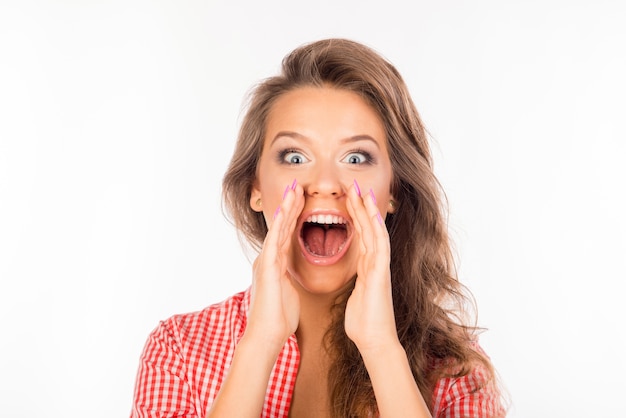 Cheerful young woman in shirt holding hands near mouth shouting