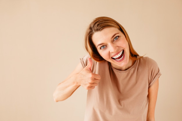 Cheerful young woman smiling and looking at camera while showing thumb up gesture 