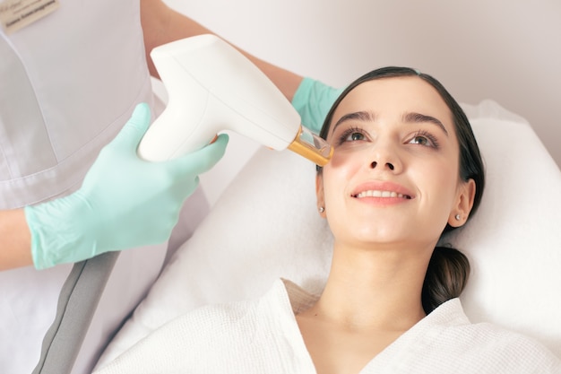 Cheerful young woman smiling while undergoing the laser treatment on her face