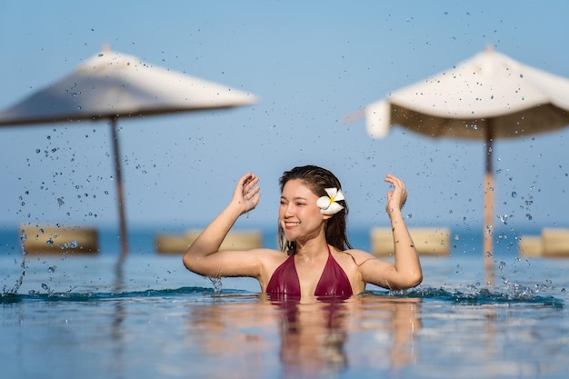 Веселая молодая женщина в купальнике, играющая в воду, плещущуюся в бассейне на фоне моря