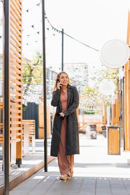 Cheerful young woman talking on a mobile phone while walking along a city street in spring