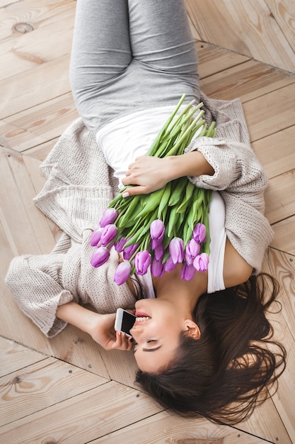 Photo cheerful young woman talking on the phone and holding flowers. beautiful lady with tulips