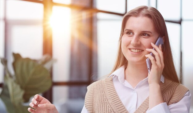 オフィスでスマートフォンで話している陽気な若い女性