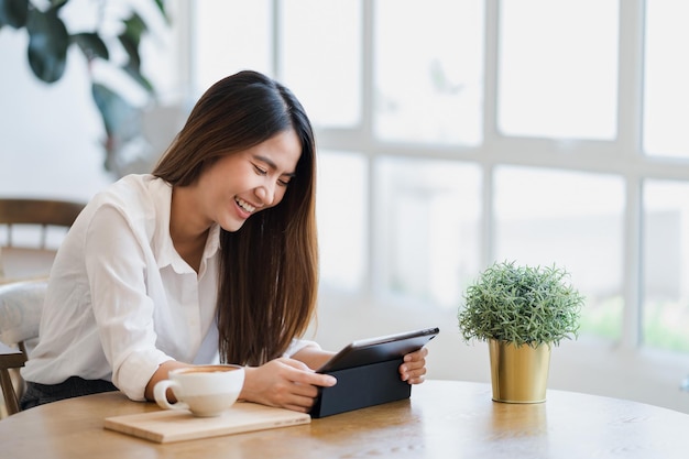 cheerful young woman using digital tablet while having coffee at table in cafe