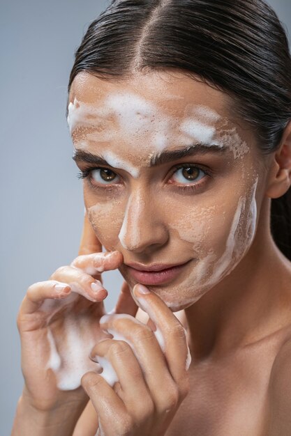 Cheerful young woman using foam for facial