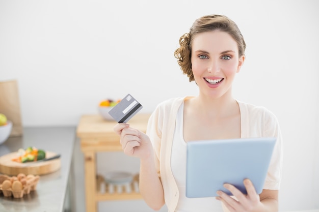 Cheerful young woman using her tablet for home shopping sitting in her kitchen