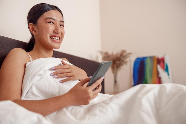 Cheerful young woman using smartphone at home