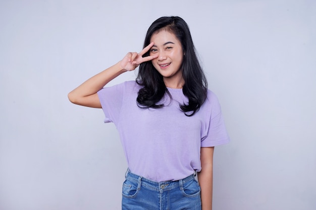 A cheerful young woman wearing casual t shirt standing isolated over white wall, showing peace gesture