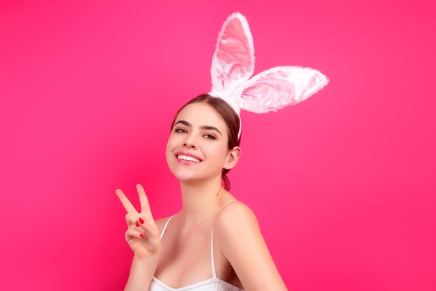スタジオの背景に装飾的な着色された卵を保持しているイースターのバニーの耳を身に着けている陽気な若い女性