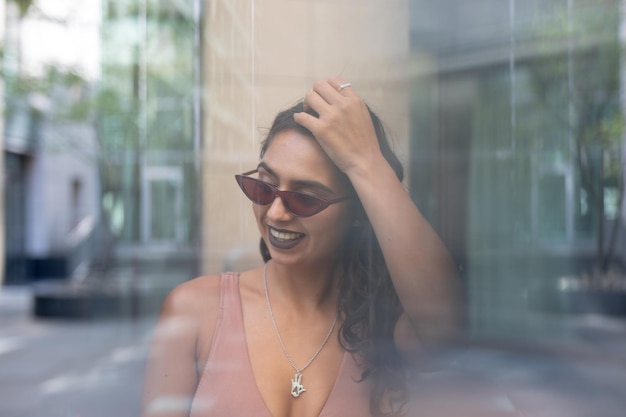 Photo cheerful young woman wearing sunglasses seen through glass window in city