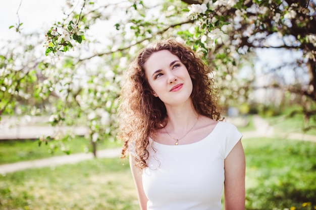 Cheerful young woman in a white t-shirt under the blooming tree.