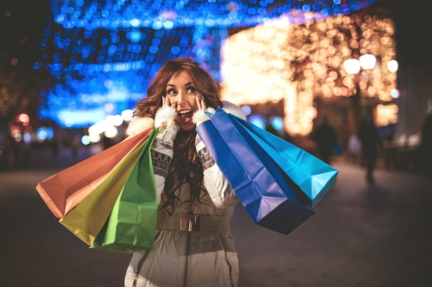 写真 クリスマスの時期に街の通りで楽しんでいるカラフルな買い物袋を持つ陽気な若い女性。