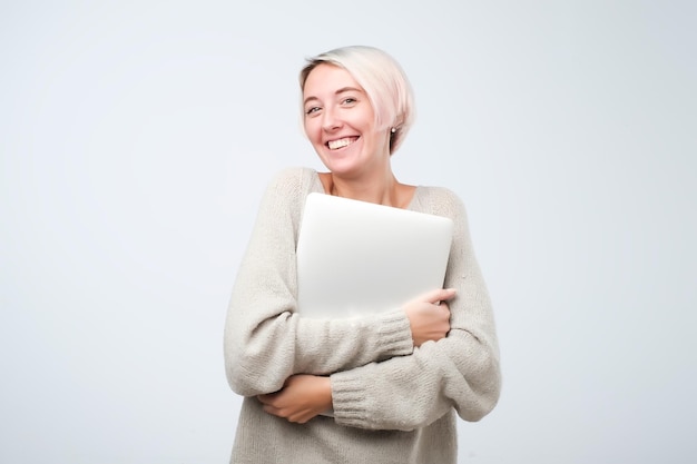 Cheerful young woman with dyed short hair standing holding laptop computer making presentation