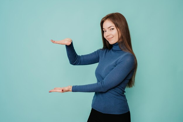 Cheerful young woman with long loose hair in blue sweater black pants holds an imaginary object