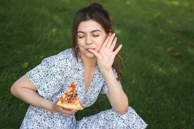 피크닉에서 피자 한 조각을 들고 쾌활한 젊은 여성