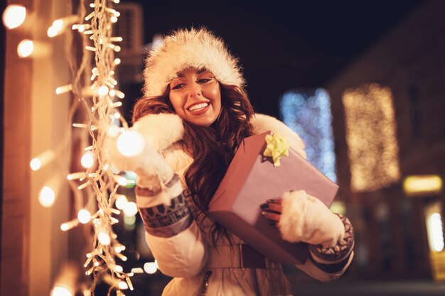 Cheerful young woman with present having fun in the city street at the Christmas time.