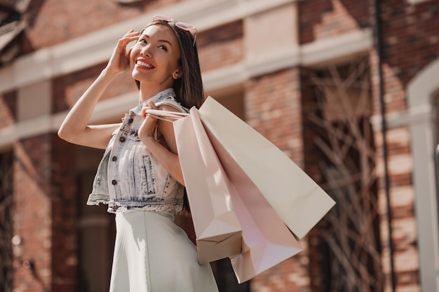 写真 屋外の肩に買い物袋を持つ陽気な若い女性