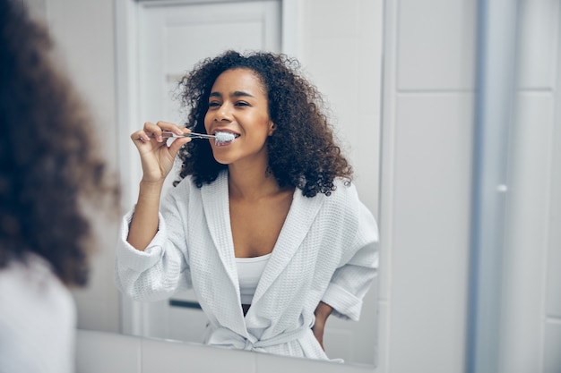 Cheerful young woman with a toothbrush in her hand looking at herself in the mirror