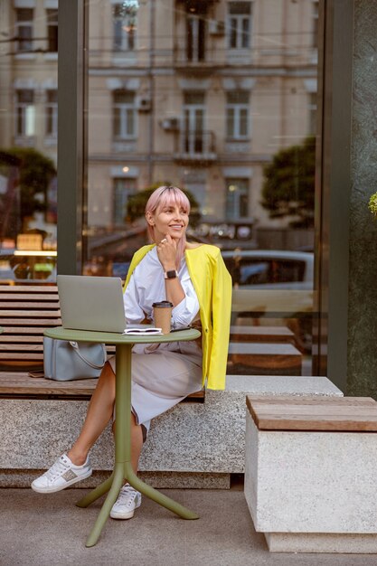 Giovane donna allegra che lavora al computer portatile al caffè all'aperto