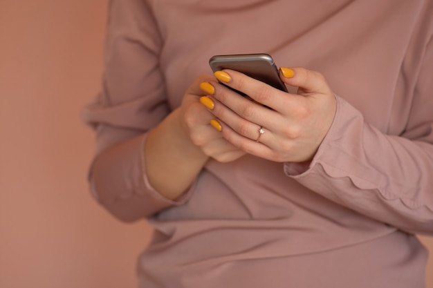 Cheerful young woman writes a text message with her mobile. Pretty young woman using smart phone. Young hipster holding mobile phone and looking at the screen.