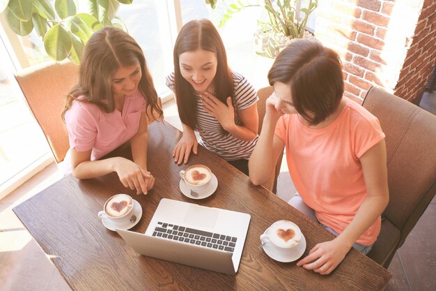 ノートパソコンでカフェに座ってコーヒーを飲む陽気な若い女性