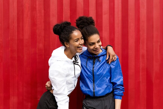 Photo cheerful young women standing against red cargo container