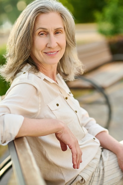 Photo cheerfulness. confident adult good looking woman smiling relaxed sitting on bench in green park