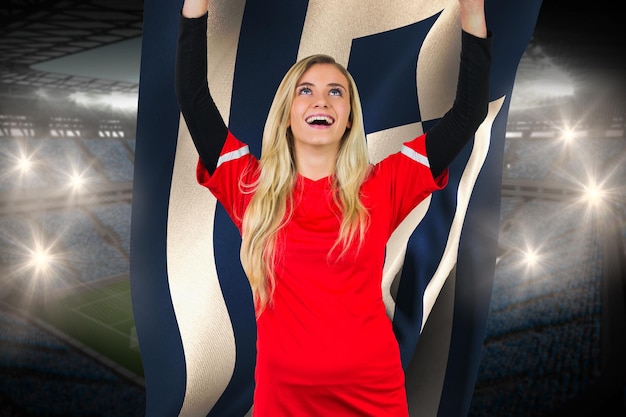 Cheering football fan in red holding greece flag against large football stadium with fans in blue