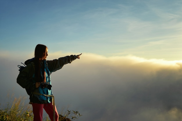 Cheering woman hiker open arms at mountain peak