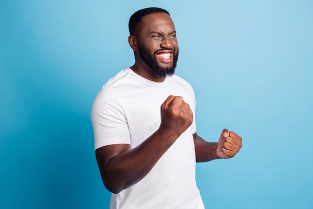 Cheering young man raise fists beaming smile over blue background