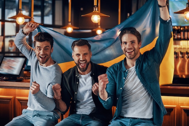 cheering young men carrying Ukrainian flag and smiling