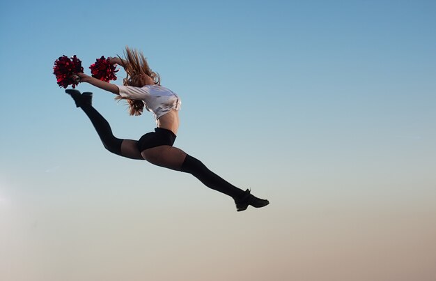 Cheerleademeisje met pompoms voert acrobatisch element in openlucht op het dak uit